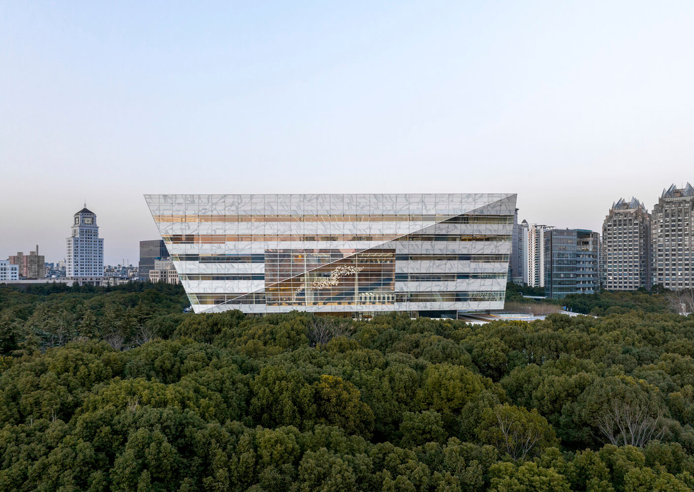Modern glass building surrounded by trees in an urban landscape.