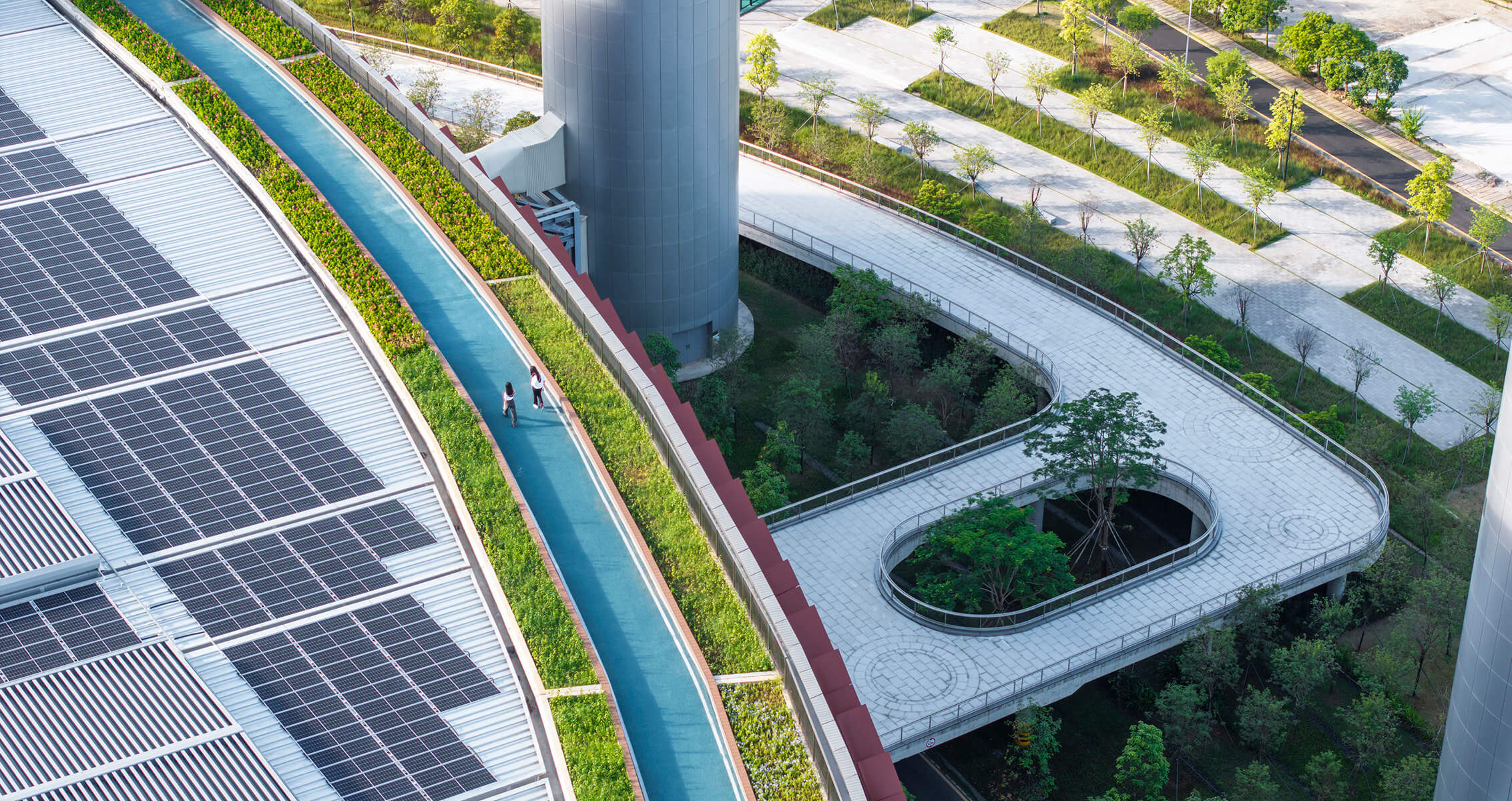 Green rooftop with solar panels and walkway, surrounded by lush trees.