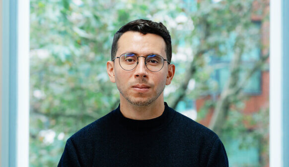 Person with glasses in front of a window with trees in the background.