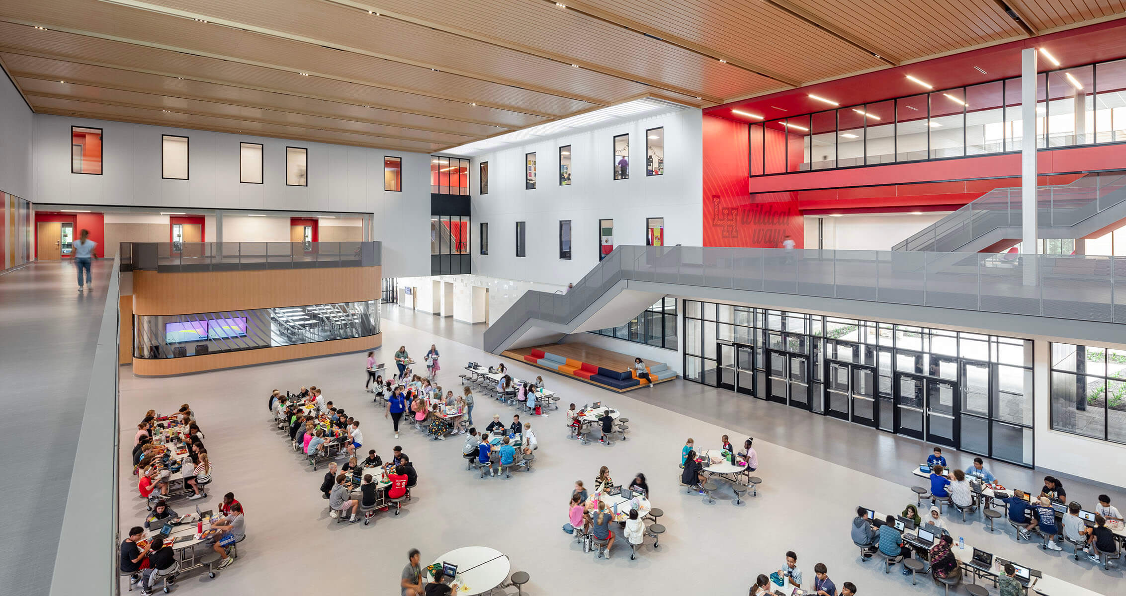 Spacious modern school cafeteria and atrium with students seated at round tables, open layout.