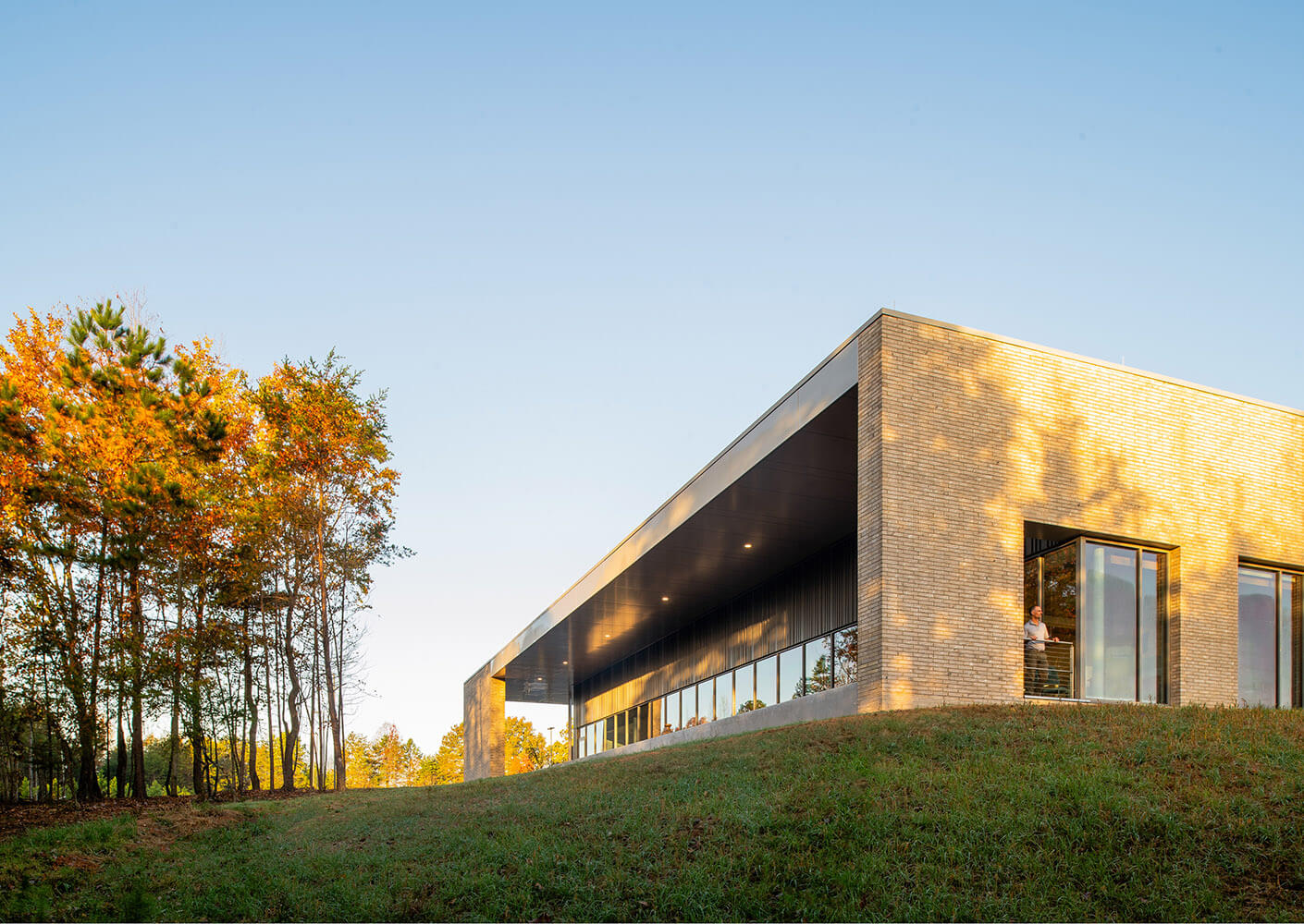 Modern brick building at sunrise with autumn trees by its side.