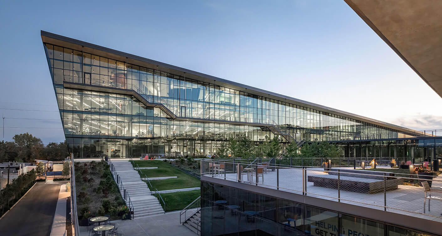 Modern glass office building at dusk with landscaped outdoor area.