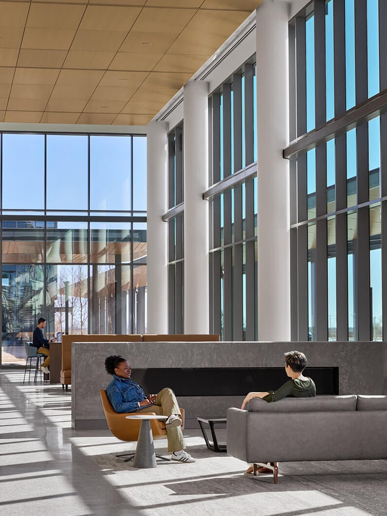 Two people talking, surrounded by large windows and natural light in the hospital lobby