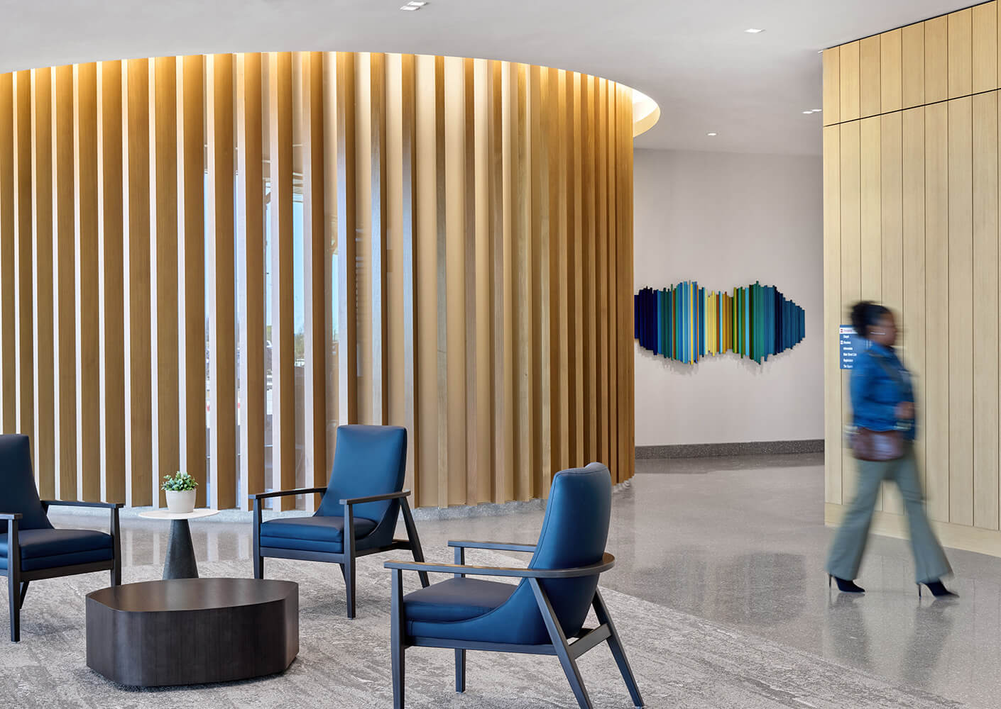 Modern lobby with blue chairs, vertical wooden panels, and colorful wall art.