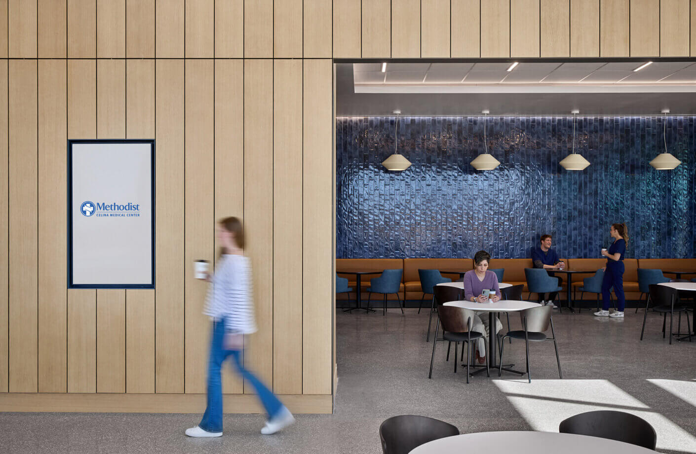 Modern dining area with a dark blue tile background in Methodist Celina Medical Center with people relaxing and drinking coffee.