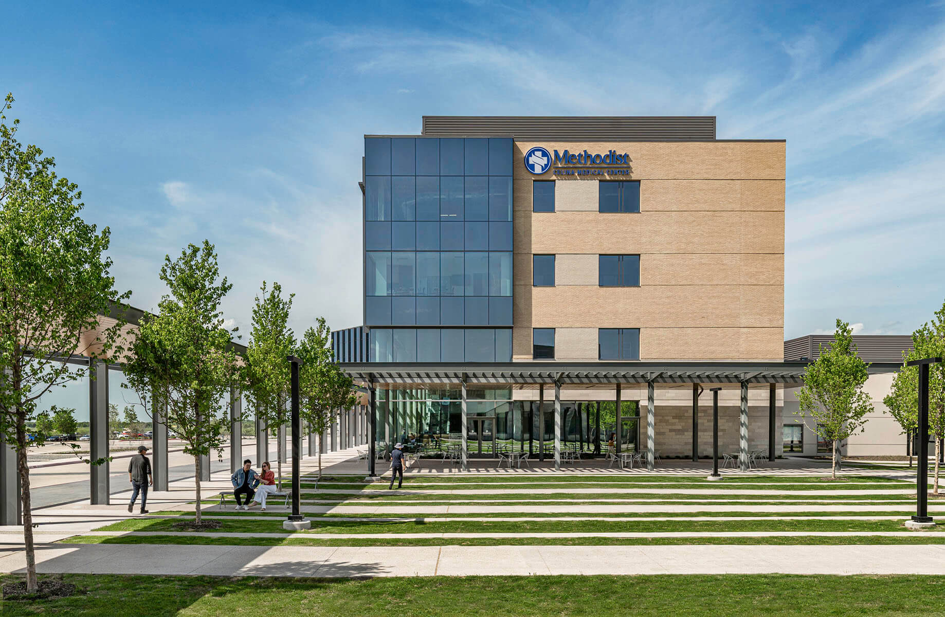 Modern hospital building with glass windows and outdoor seating area with trees and grass