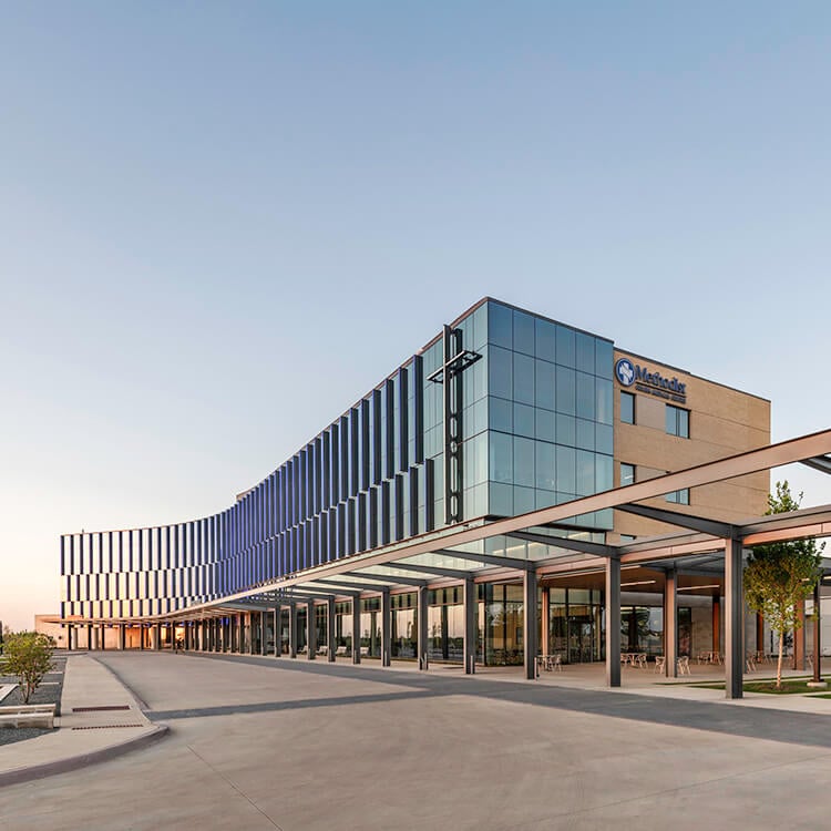 Modern glass hospital under clear sky at sunset.