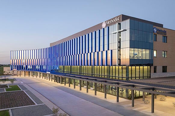 Modern hospital building exterior at dusk with glass facade and clear sky.