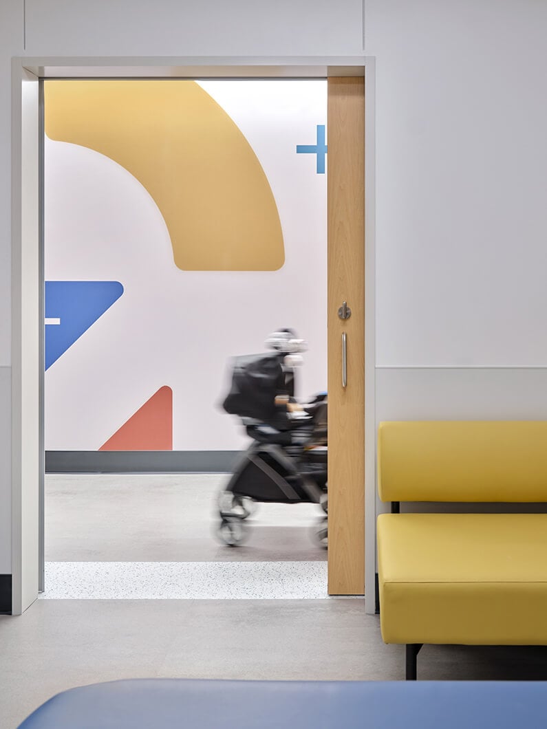 Modern hospital hallway with colorful, abstract wall art visible from patient room with its door open