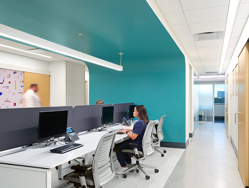 Modern office space with turquoise walls and employees at desks, open to door-lined hallways on both sides