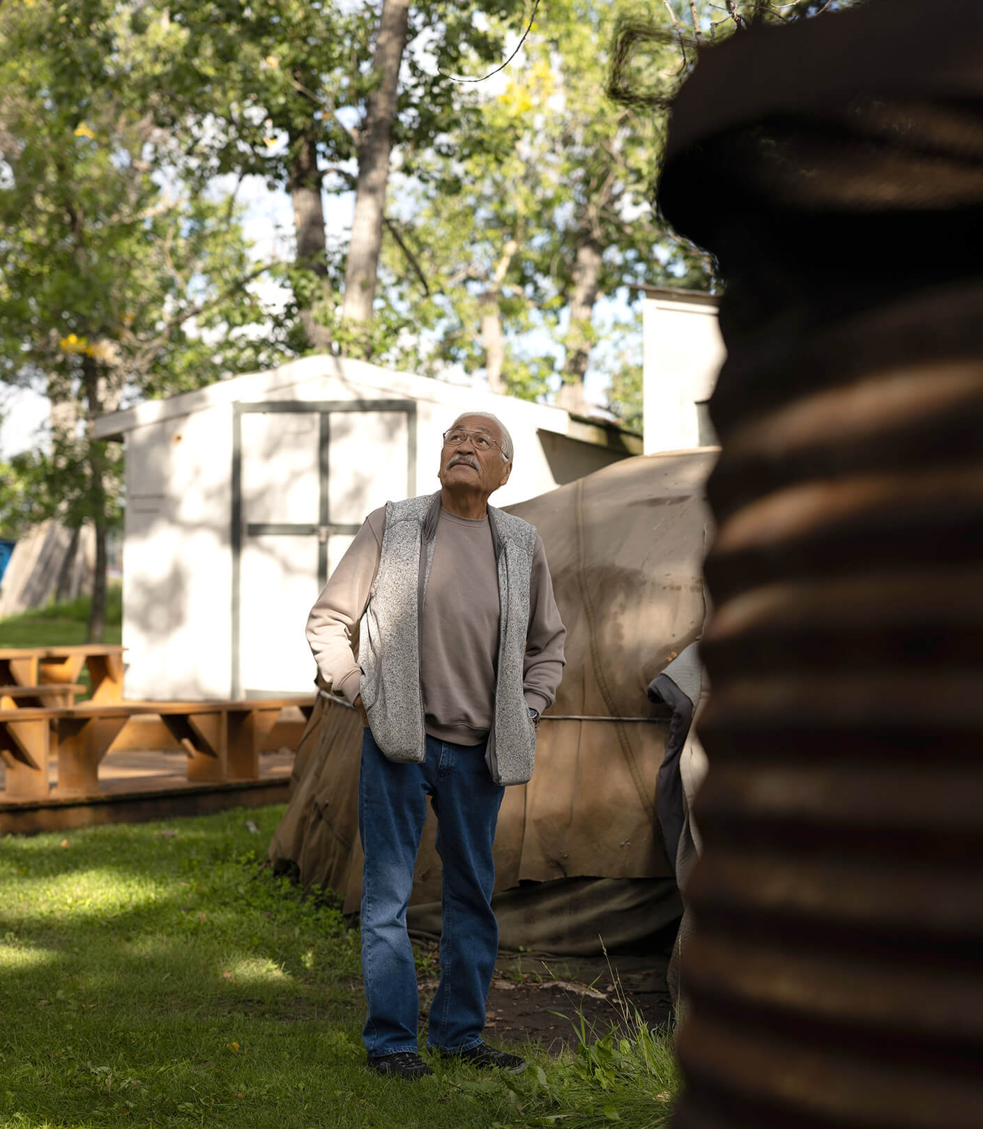 Older man looking up in a forested area with white outbuildings
