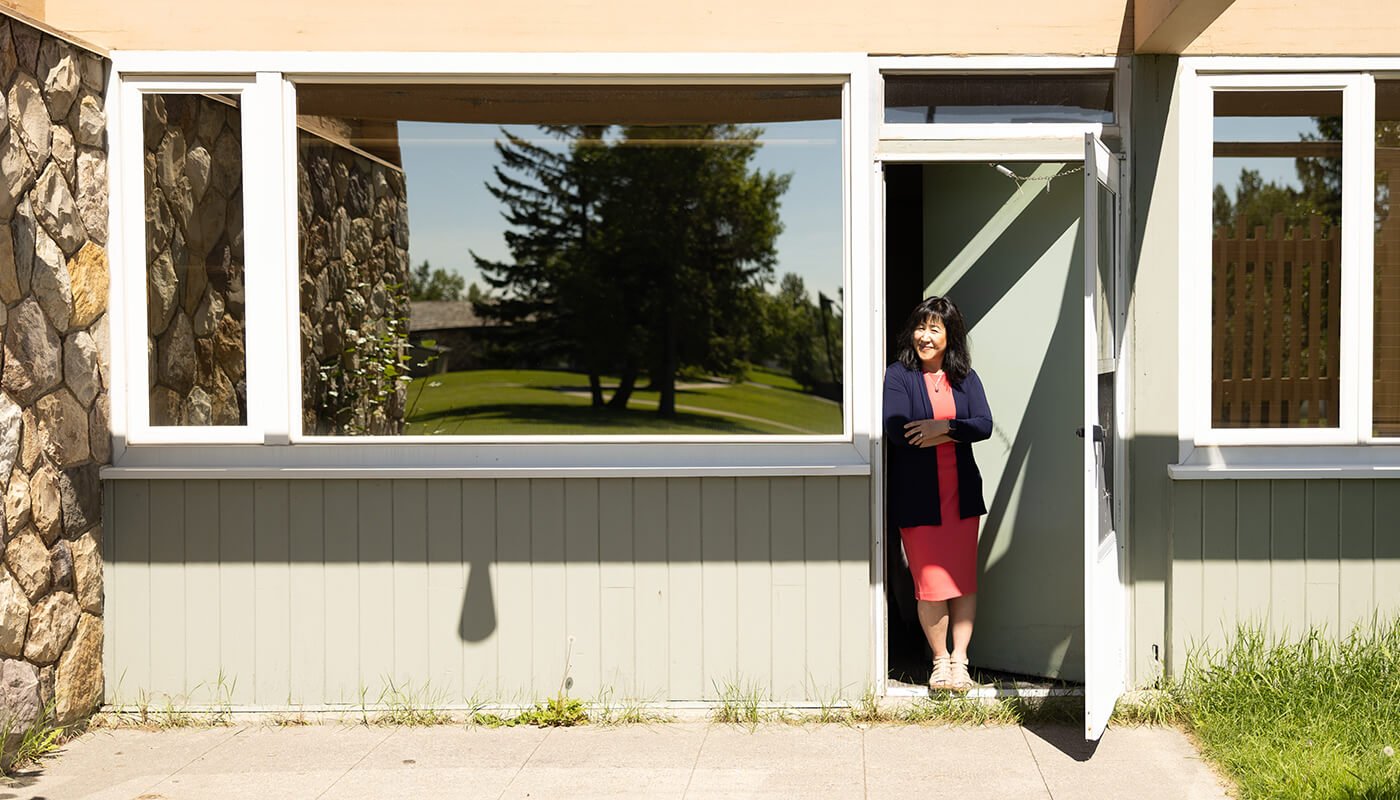 Smiling woman standing in doorway with trees reflecting in the window.