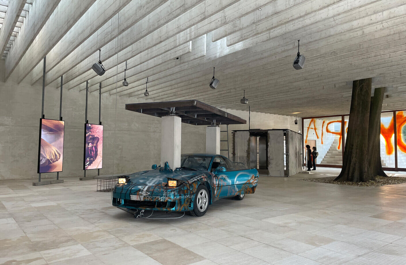 Exhibit with graffiti car and digital art in a modern concrete gallery space.