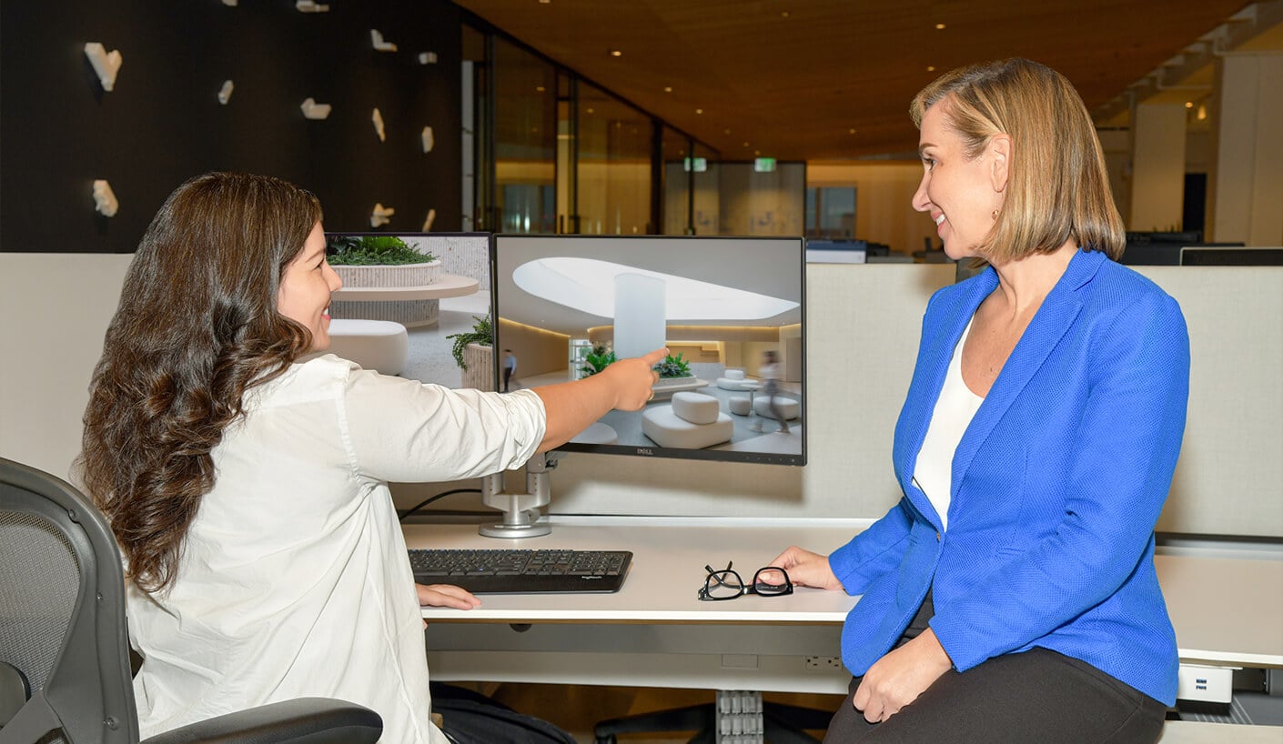 Two women discussing a design on a computer screen in a modern office setting.