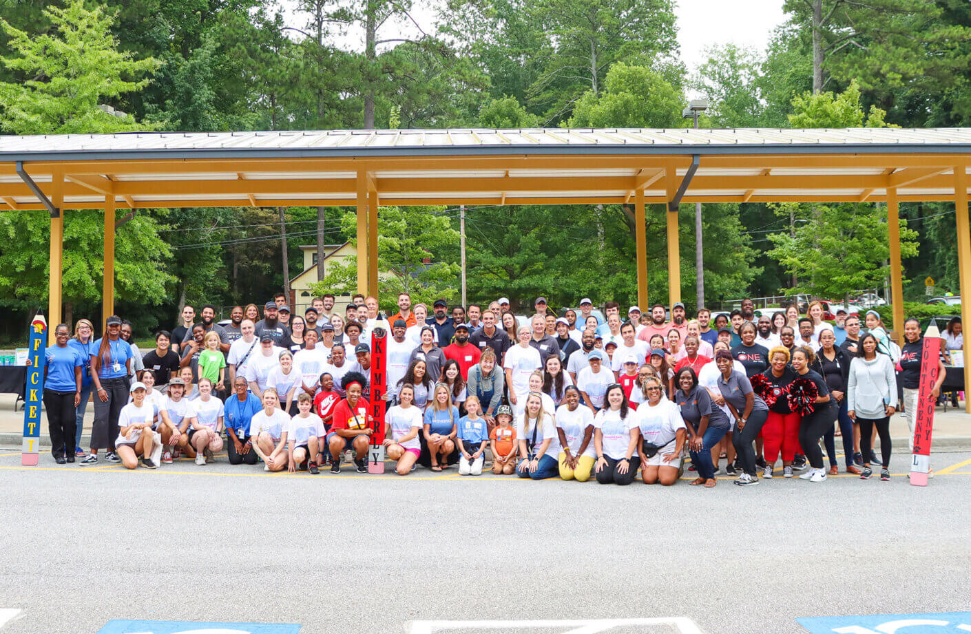Large group smiling at outdoor event with trees and pavilion.