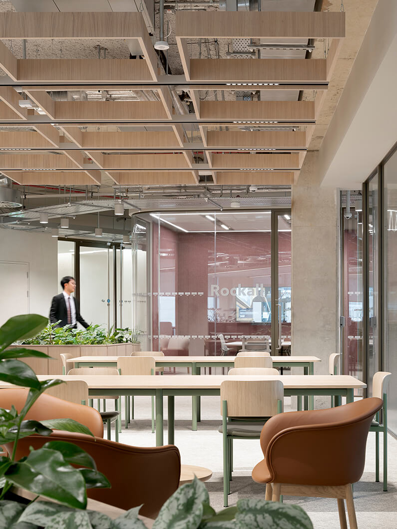 Modern office space with wooden decor and seating, plants, and a glass meeting room.