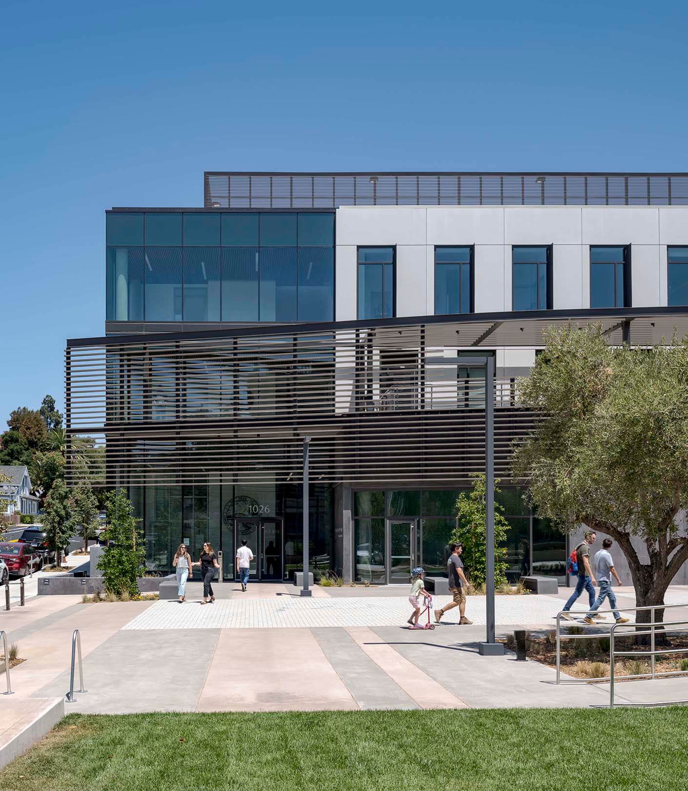 Modern office building exterior with people walking in front, sunny day.
