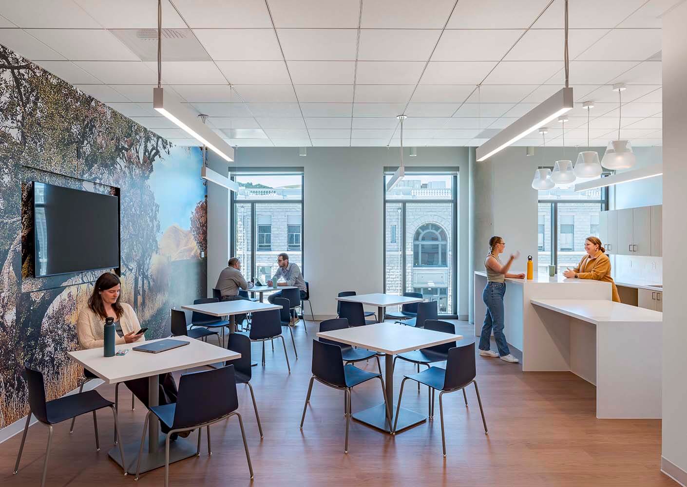 Modern office break room with people socializing and using tables.