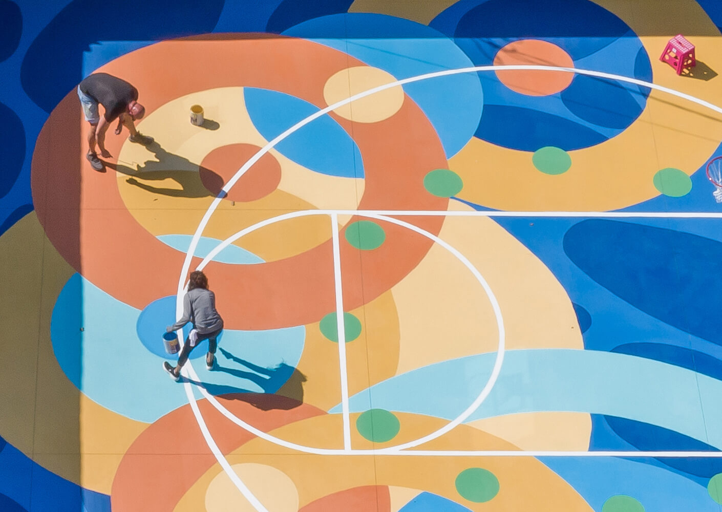 Men painting colorful basketball court mural from above.