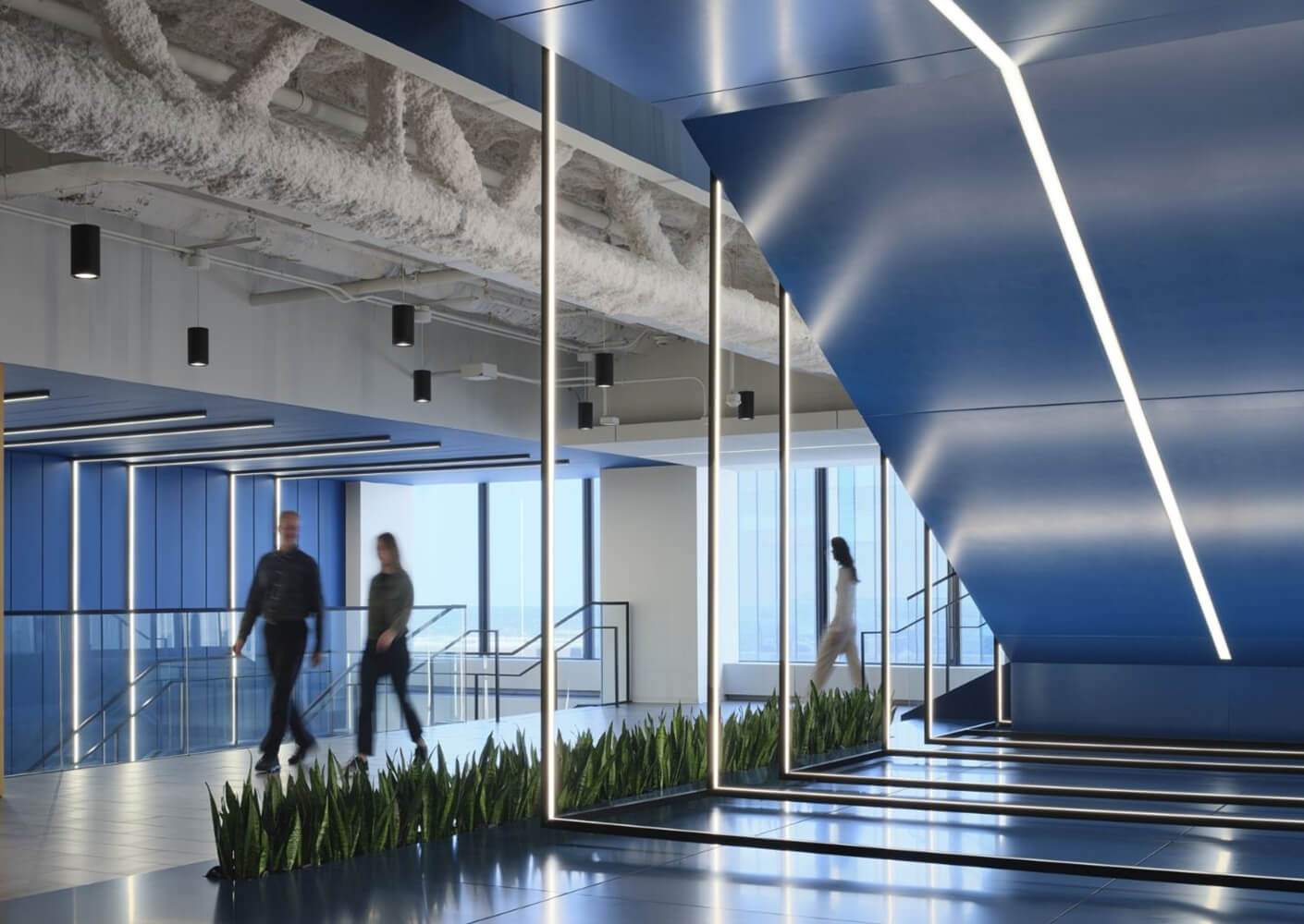 Modern office interior with blue accents and green plants, people walking.