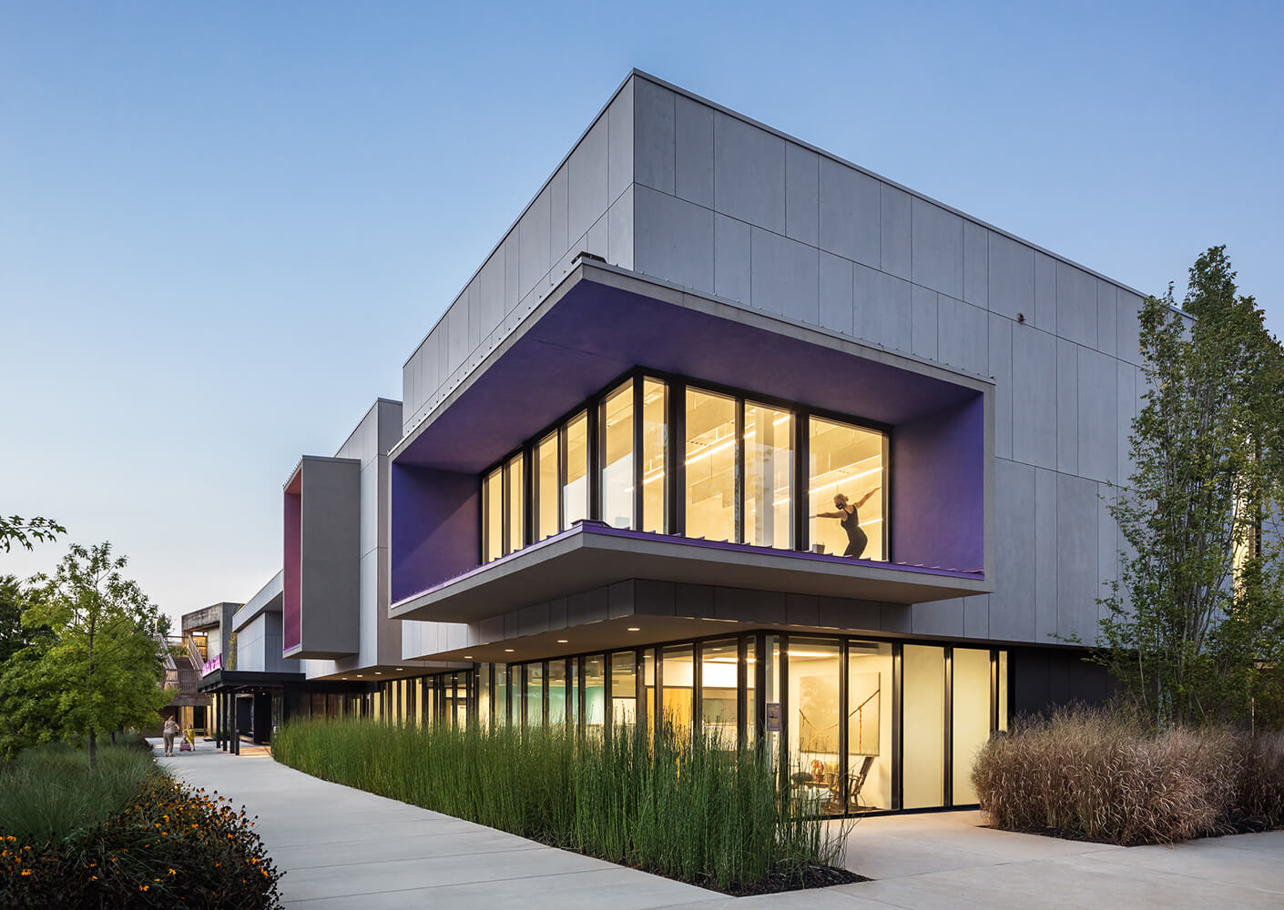 Modern building with large windows and twilight sky, silhouetted figure inside.