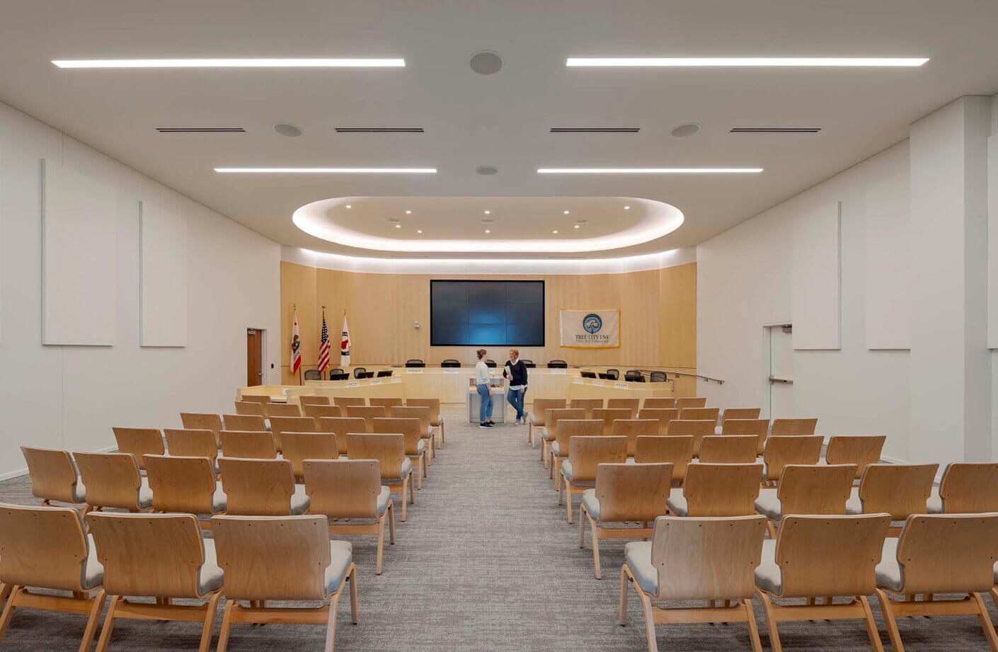 Modern meeting room with rows of chairs and large screen at the front.