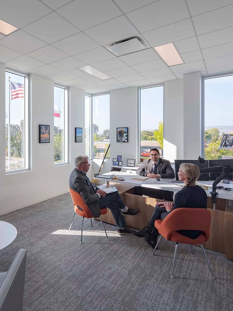 Office meeting with three people discussing at a desk in a modern, bright room.
