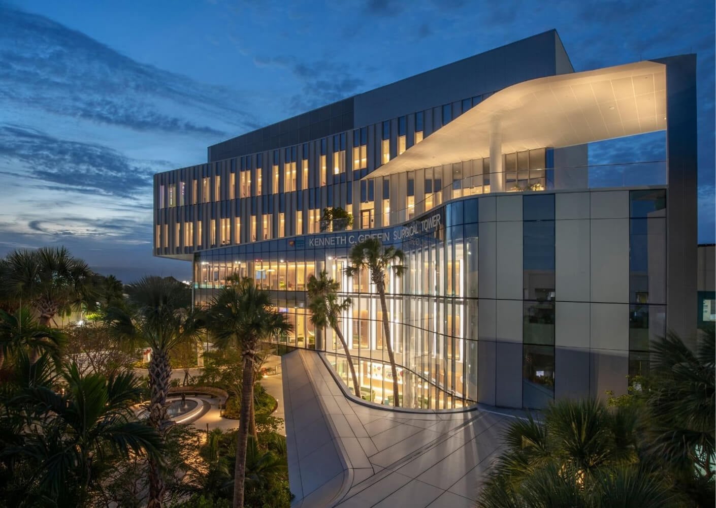 Modern building with illuminated windows and palm trees at dusk.
