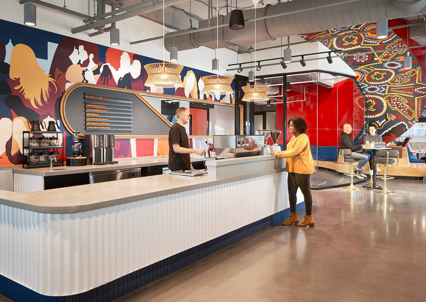 Modern office kitchen with vibrant wall art and people socializing.