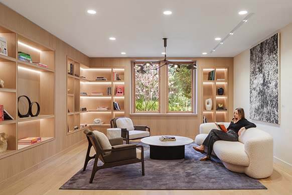 Modern cozy living room with bookshelves and woman reading on a sofa.