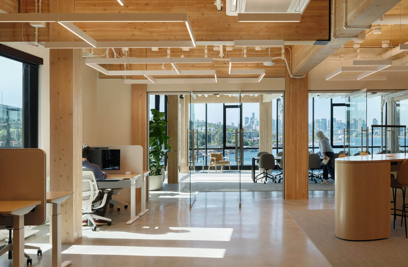 Modern open office with city skyline and water views, featuring wood accents and natural light.