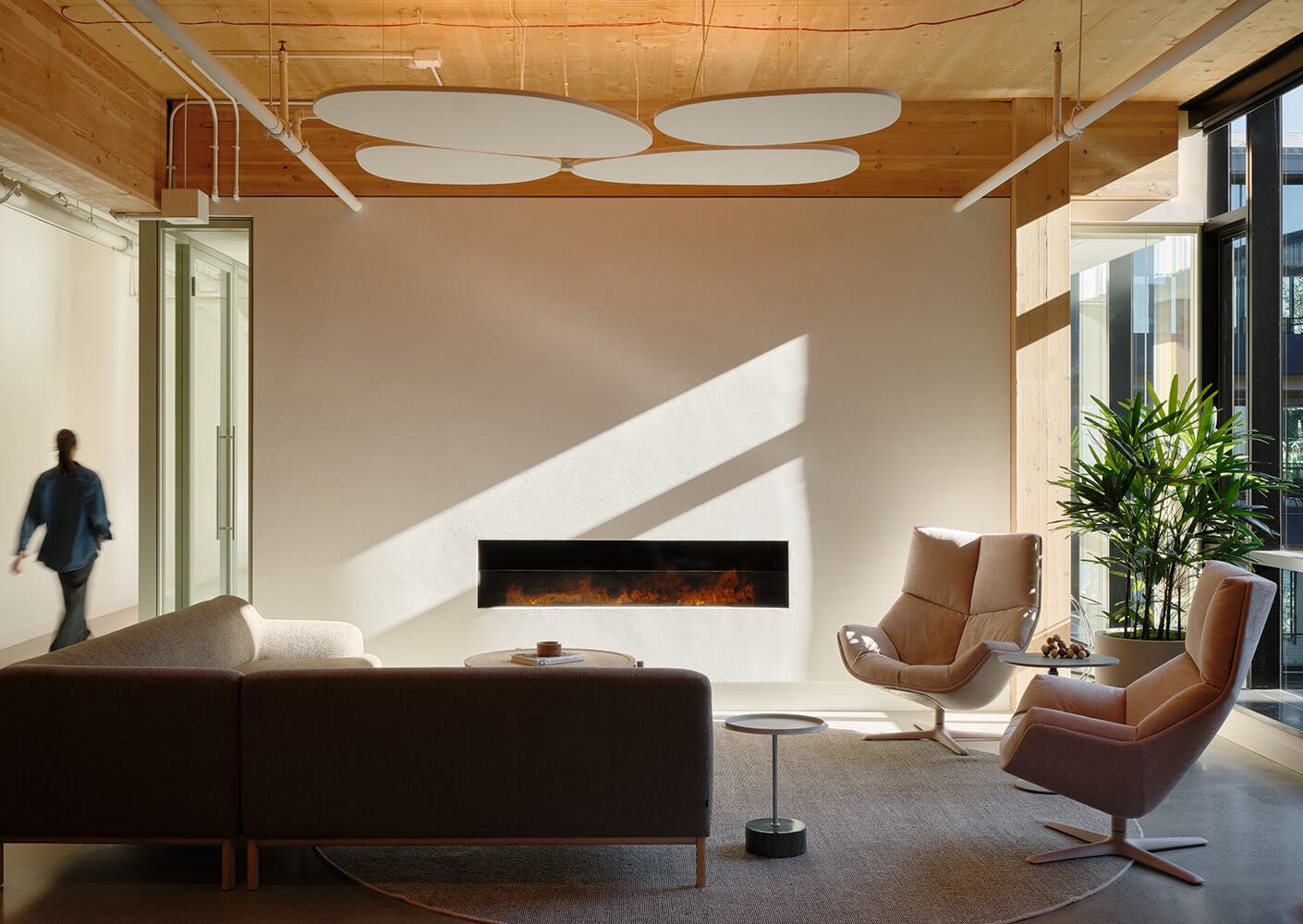 Modern office lounge with sofa, armchairs, fireplace, and natural light.