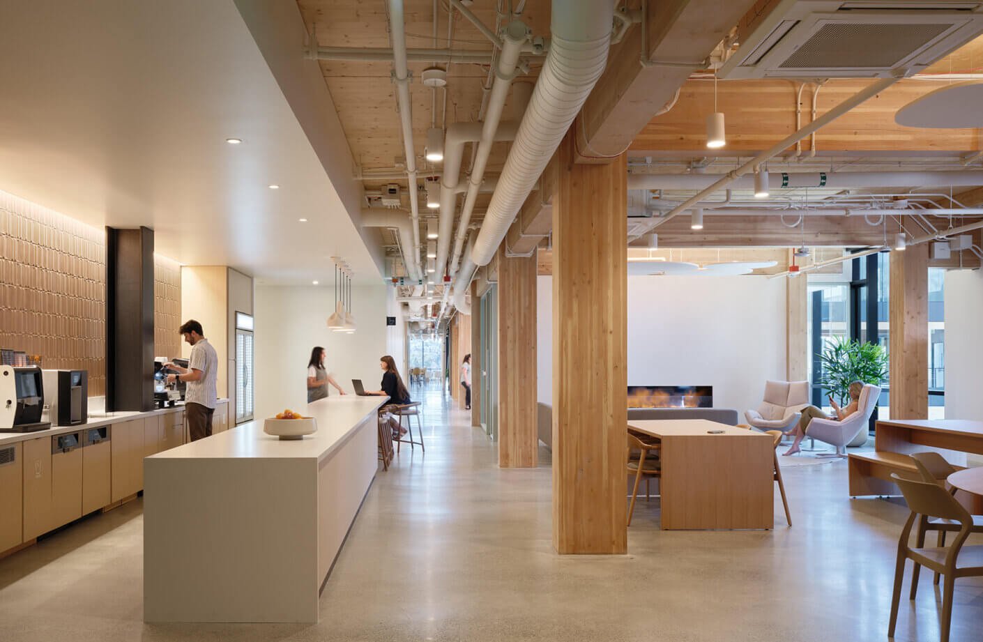 Modern office lounge with wooden accents and people working, chatting, and relaxing.