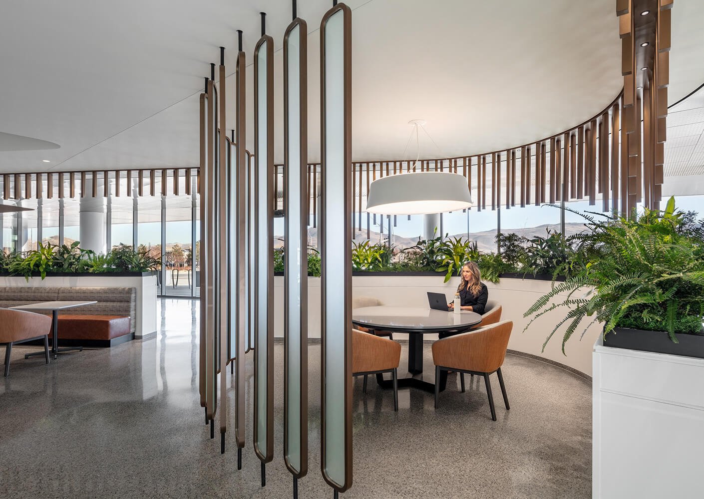 Decorative vertical panels and plants encircle a round table where a woman works on a laptop.