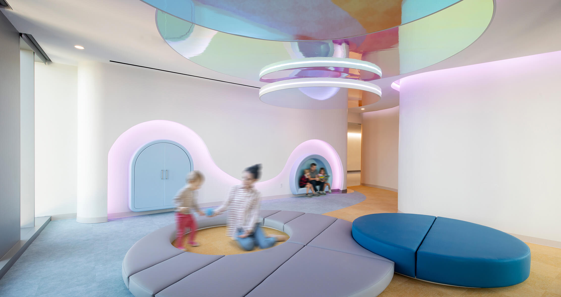 Children and caretakers play in a colorful room with rounded, soft play mats and nooks