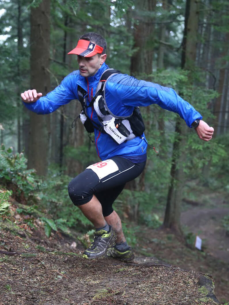 Trail runner in blue jacket racing through a forest.