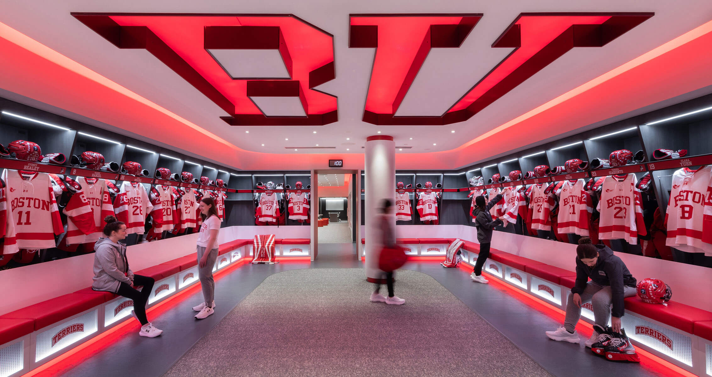 Boston University hockey women's ice hockey locker room with jerseys and helmets displayed.