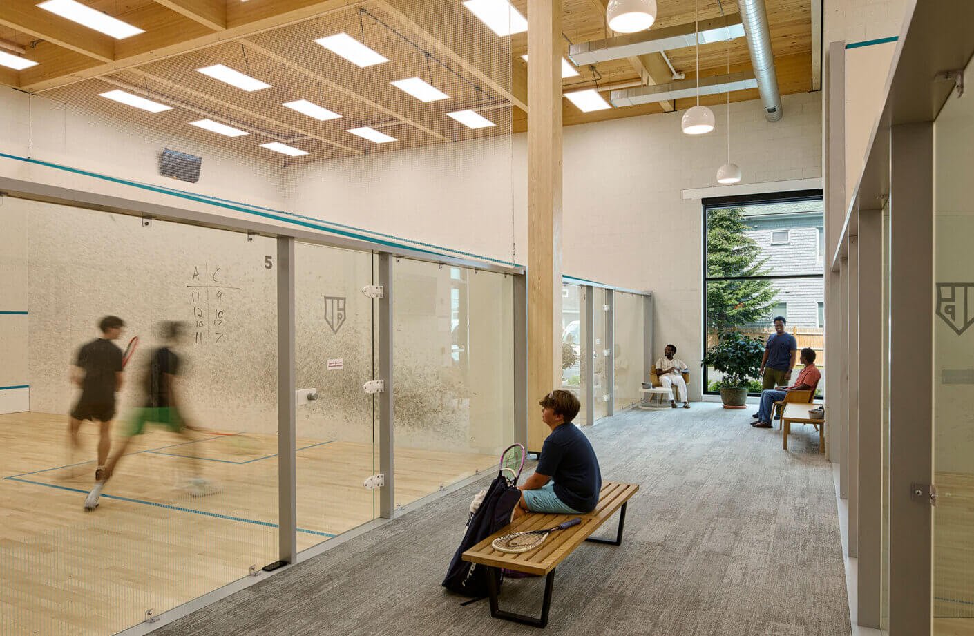 Modern squash courts with players and spectators inside a bright community squash sports facility.