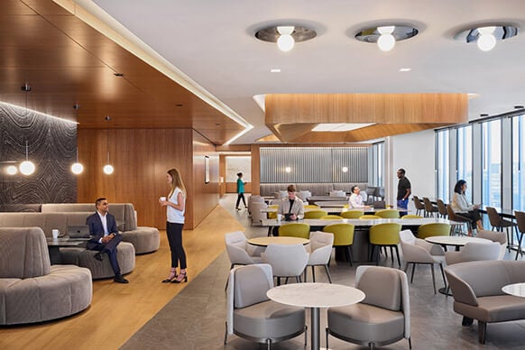 Modern office cafeteria with stylish seating and people engaging in conversation.