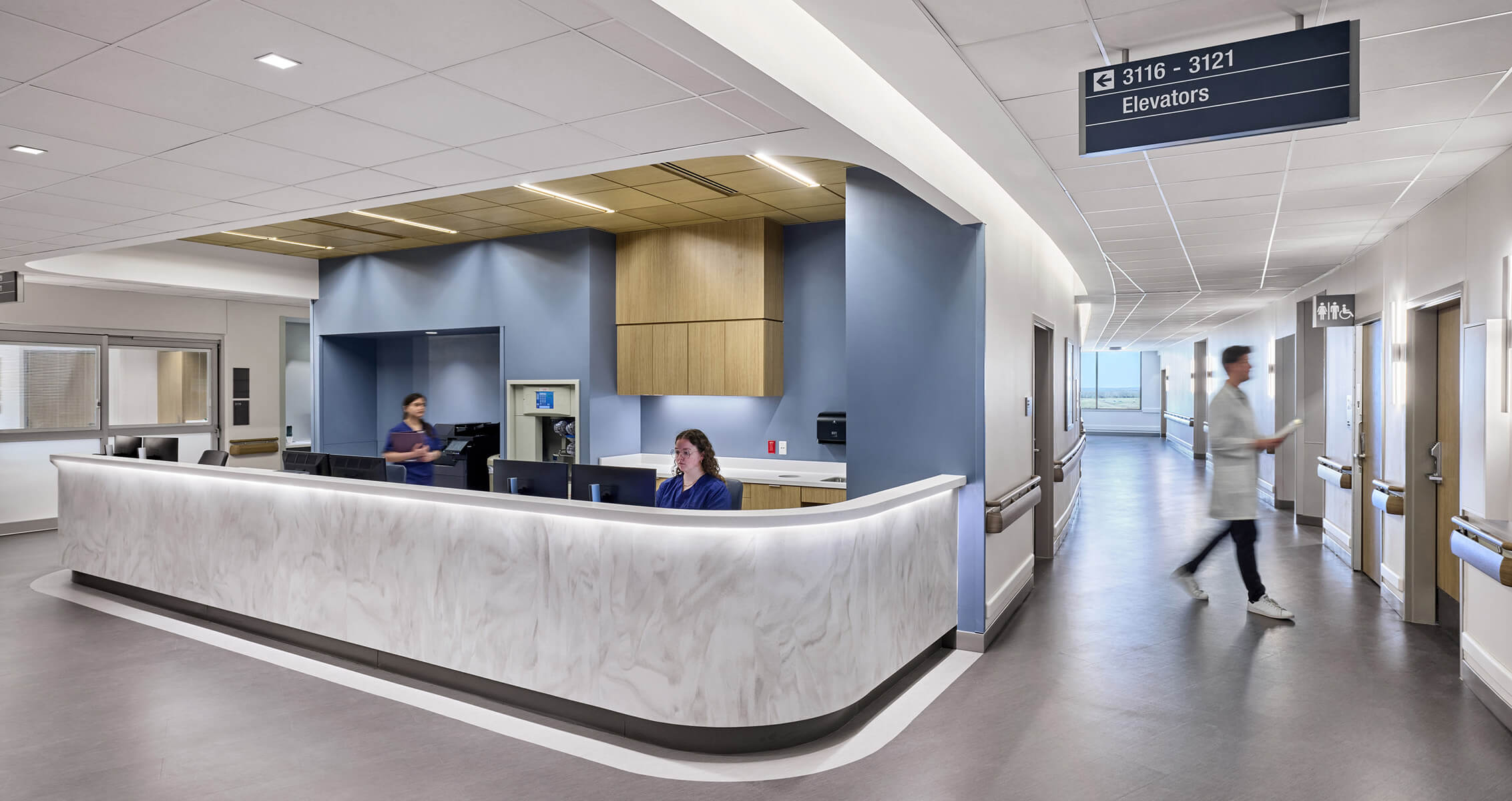 Hospital nurses station with blue back wall and staff and hallway signage.