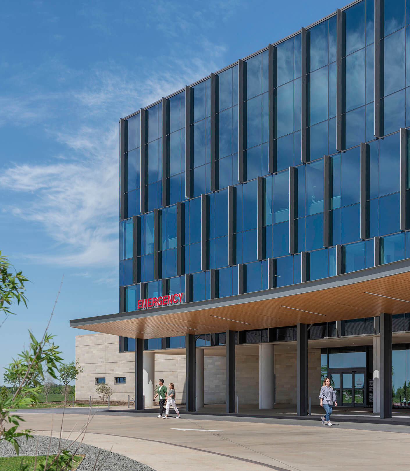 Modern hospital entrance with emergency sign under clear blue sky.