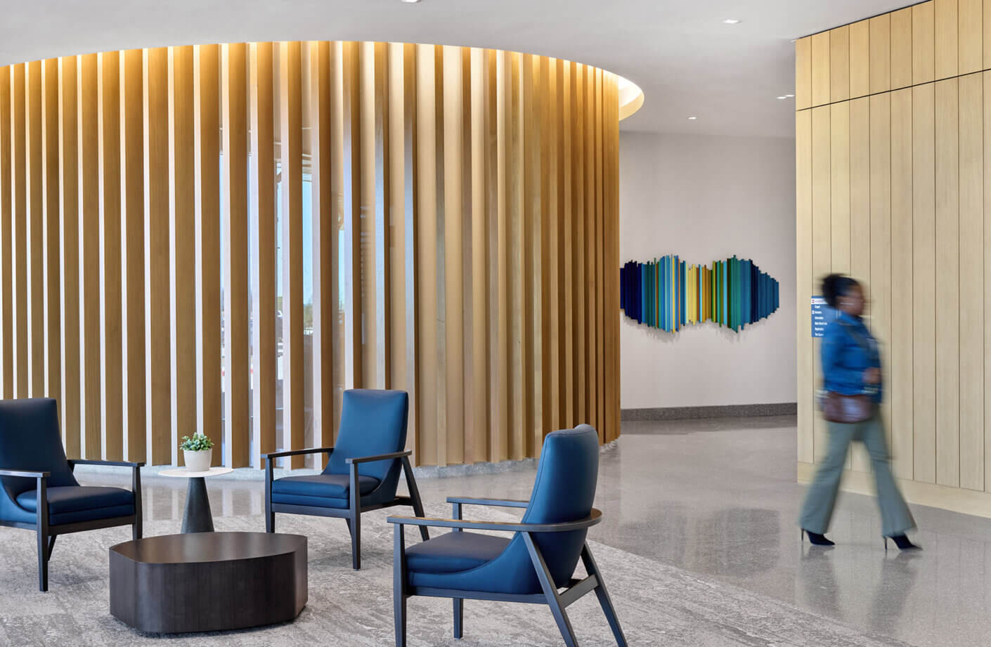 Modern lobby with blue chairs and vertical wooden fins on a curving wall.
