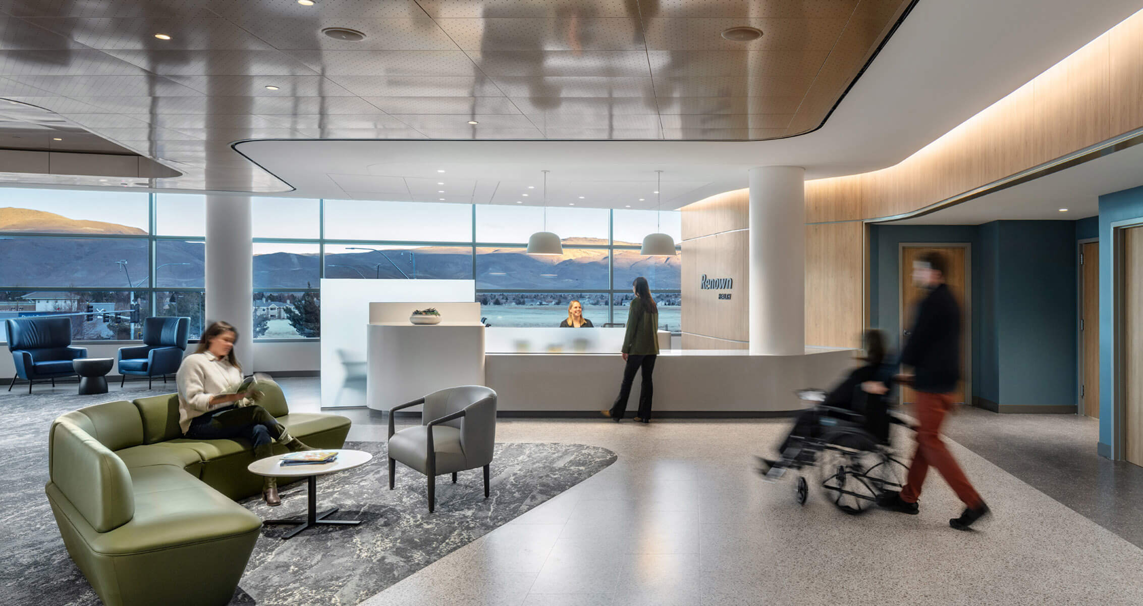 Modern hospital lobby with reception desk and visitors in a spacious, well-lit area with tall windows.
