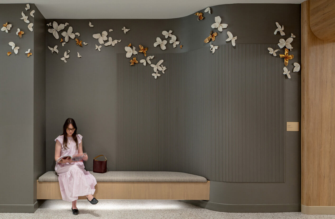Woman reading on bench with floral wall art and dark background.