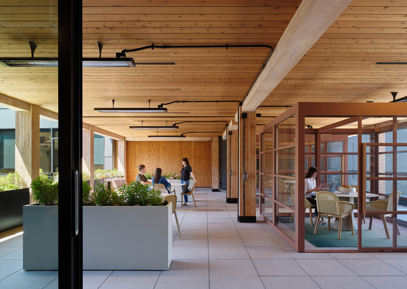 Modern office space with wooden decor, glass walls, and people collaborating.