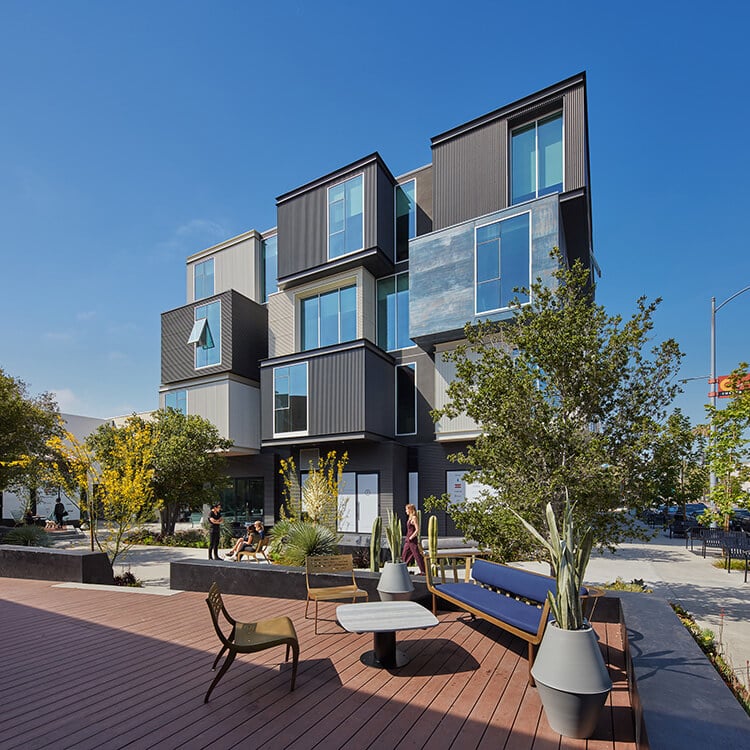 Modern stacked apartment building with outdoor seating and lush greenery.