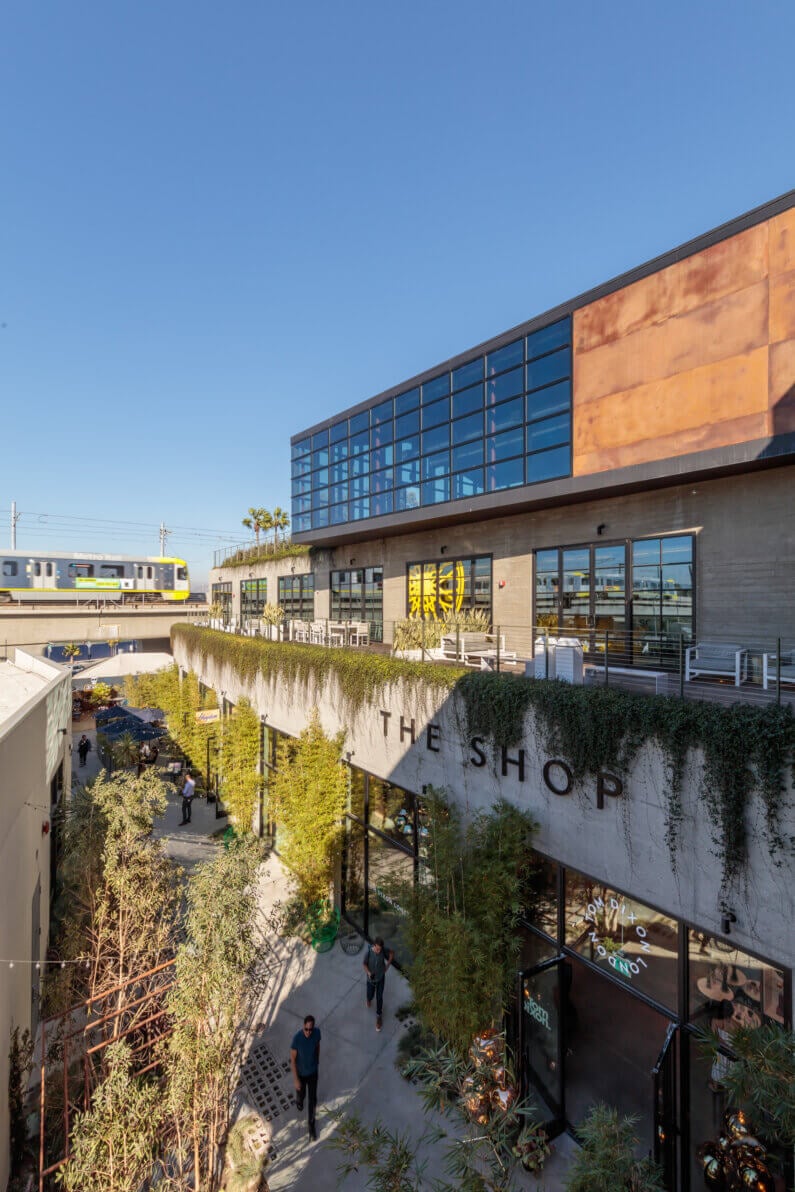Modern urban building with greenery, train passing above, sunny day.