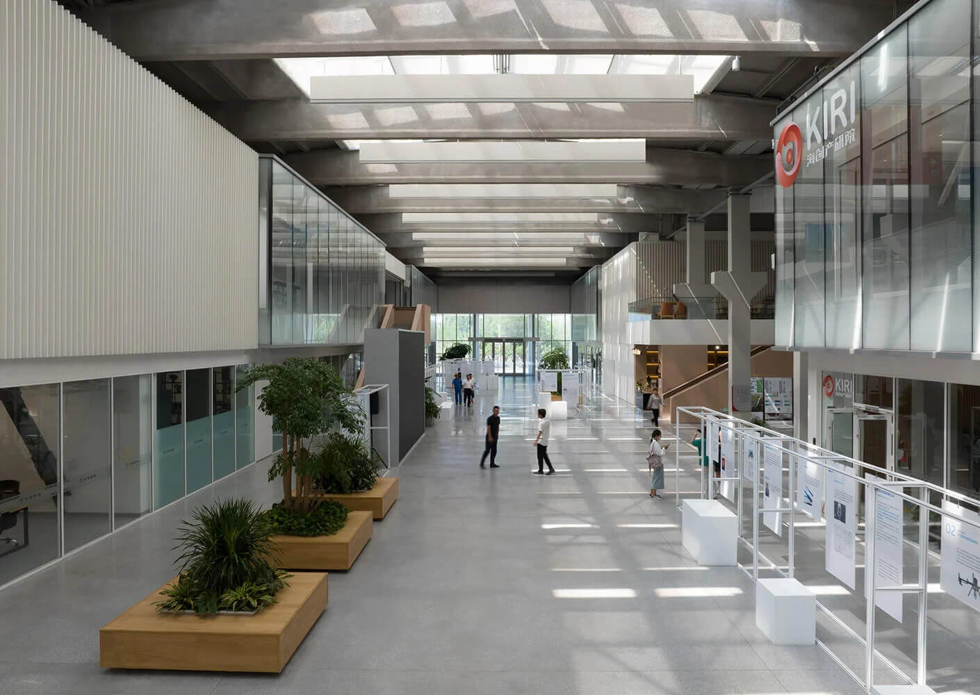 Modern office atrium with natural light, people walking, and greenery.