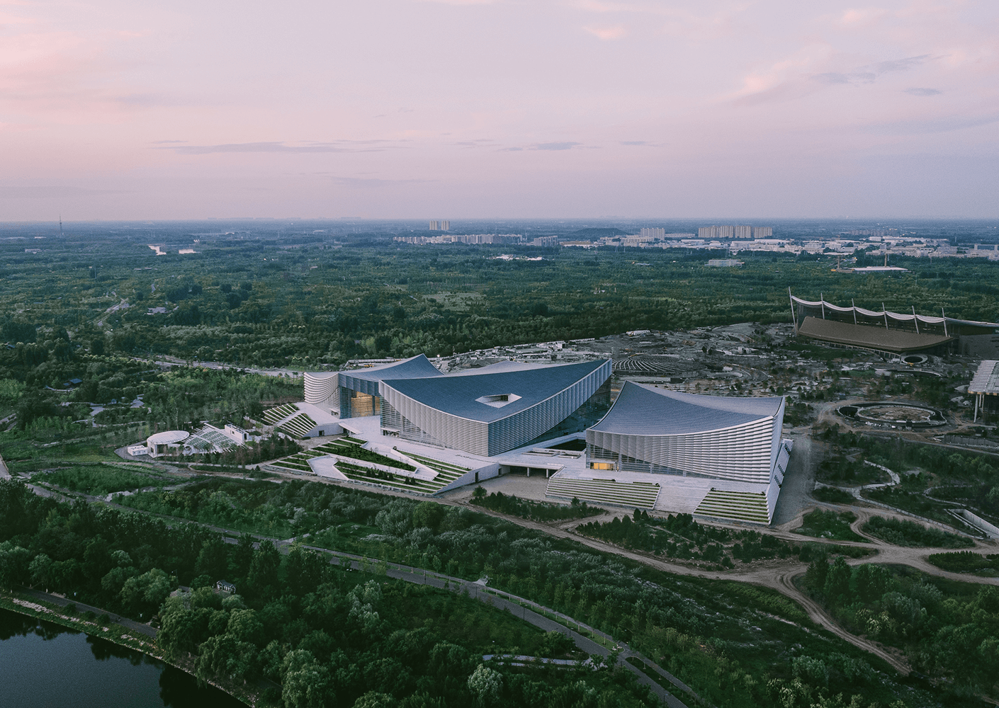 Aerial view of a modern architectural building in a green landscape at sunset.