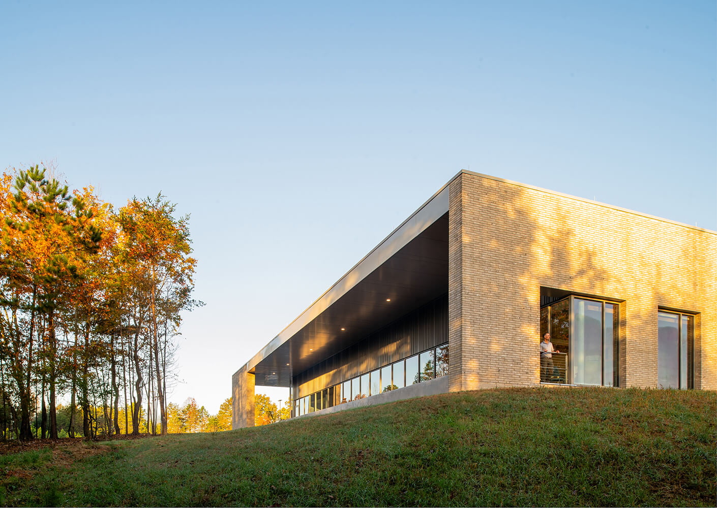 Modern building with large windows surrounded by green lawn and trees at sunset.